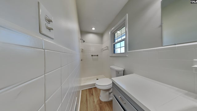 full bathroom featuring tiled shower, toilet, a wainscoted wall, wood finished floors, and tile walls