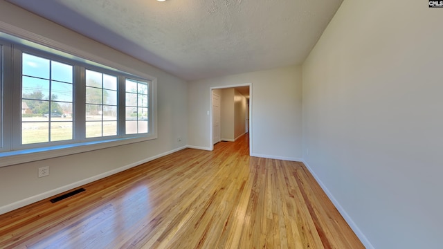 spare room featuring baseboards, visible vents, a textured ceiling, and light wood finished floors