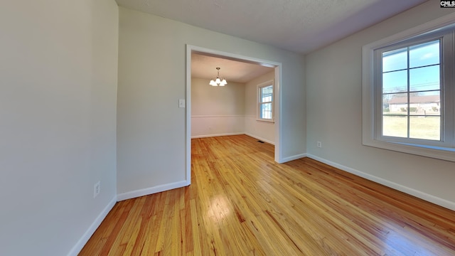 spare room featuring light wood-style flooring, baseboards, and a notable chandelier