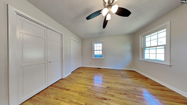 unfurnished bedroom with a textured ceiling, light wood-type flooring, a ceiling fan, and baseboards