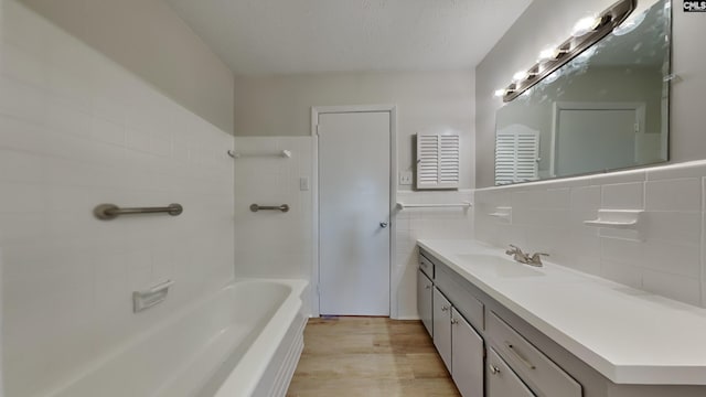 full bath with wood finished floors, a bathtub, a textured ceiling, vanity, and tile walls