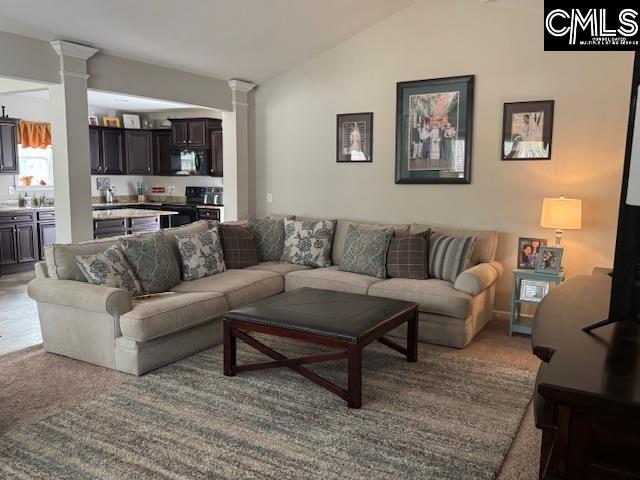 carpeted living area featuring ornate columns and vaulted ceiling