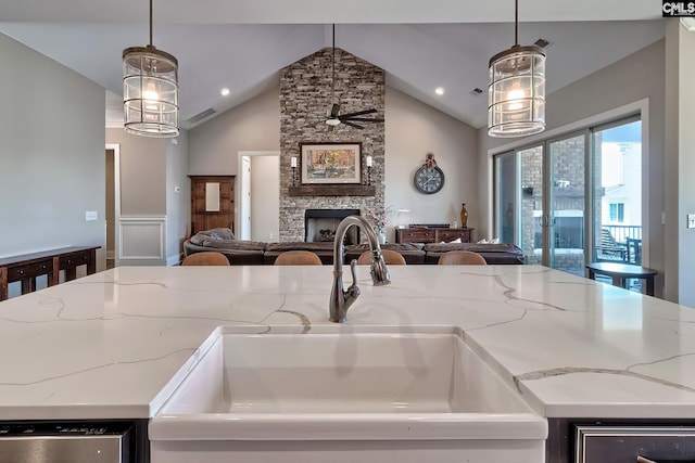 kitchen featuring open floor plan, a stone fireplace, a sink, and a kitchen island with sink