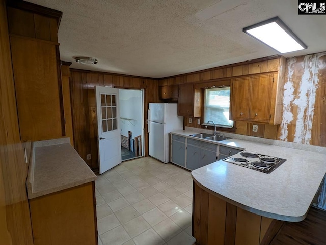 kitchen with light countertops, electric cooktop, freestanding refrigerator, a sink, and a peninsula