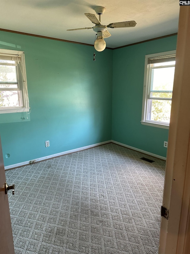 carpeted spare room featuring ornamental molding, visible vents, ceiling fan, and baseboards