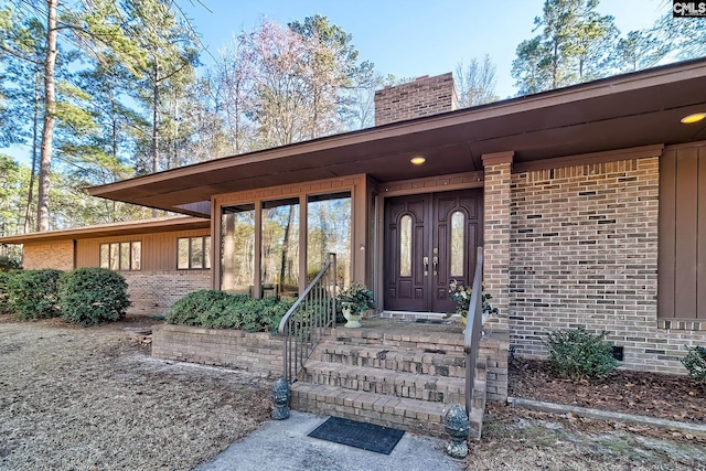 entrance to property featuring a chimney and brick siding