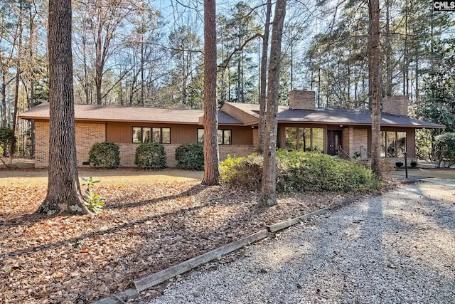 single story home with brick siding, driveway, and a chimney