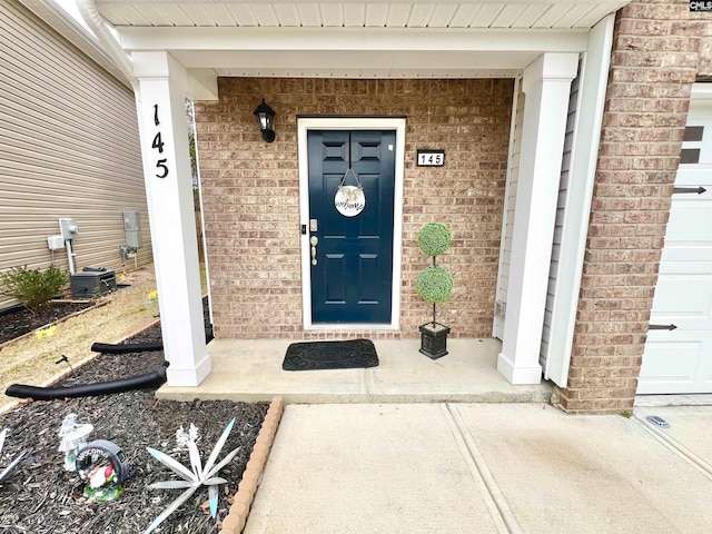 entrance to property featuring a garage and brick siding