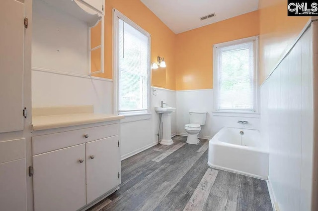 full bath with wainscoting, plenty of natural light, wood finished floors, and toilet