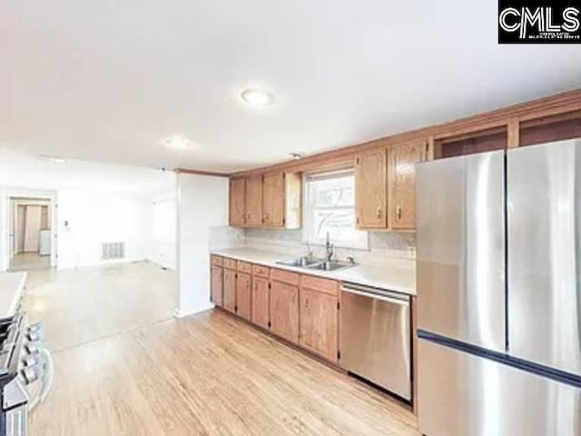 kitchen with tasteful backsplash, stainless steel appliances, light countertops, light wood-style floors, and a sink