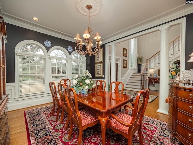 dining space with crown molding, a chandelier, stairs, and ornate columns