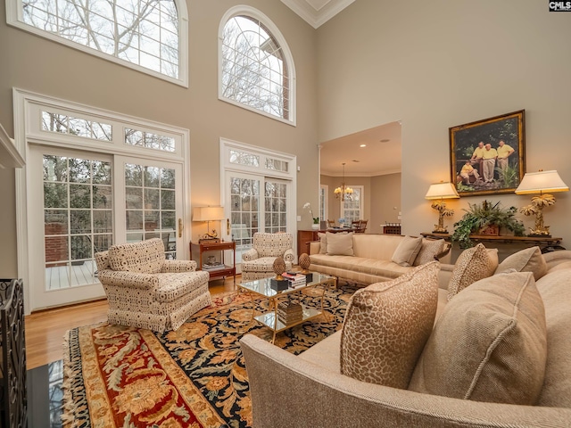 living area featuring crown molding, wood finished floors, a towering ceiling, and a notable chandelier