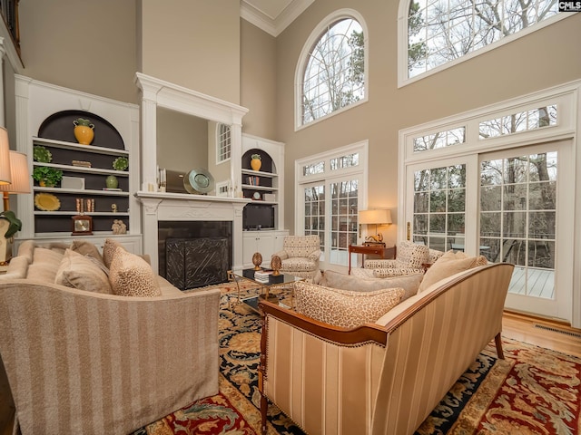 living area with visible vents, a towering ceiling, ornamental molding, wood finished floors, and a fireplace