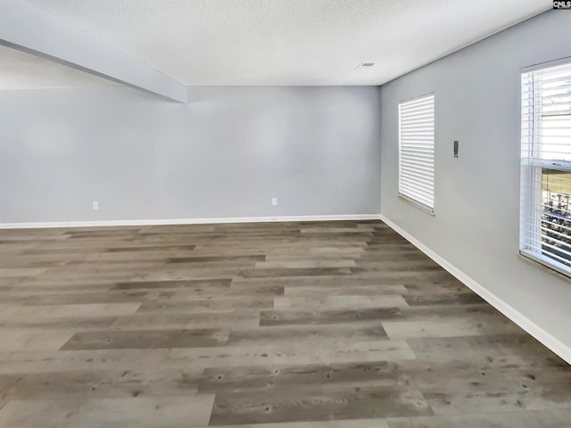 empty room with a textured ceiling, baseboards, and wood finished floors