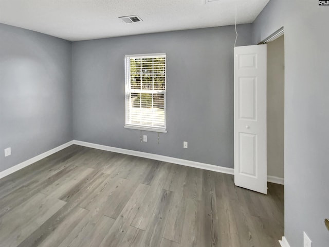 empty room featuring attic access, wood finished floors, and baseboards