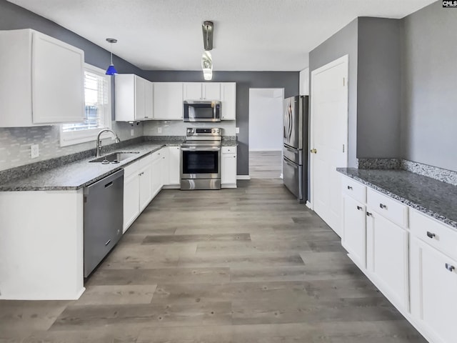 kitchen with pendant lighting, a sink, stainless steel appliances, light wood-style floors, and white cabinets