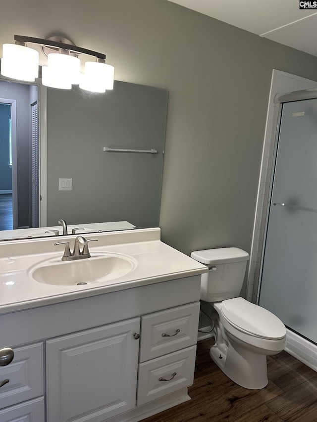 bathroom with a shower with door, toilet, wood finished floors, and vanity