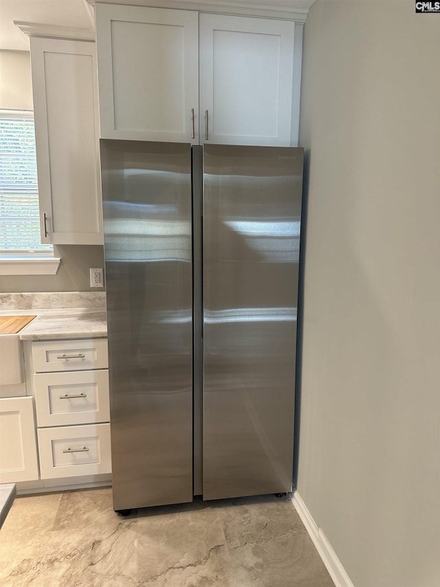 kitchen featuring white cabinetry, freestanding refrigerator, baseboards, and a sink