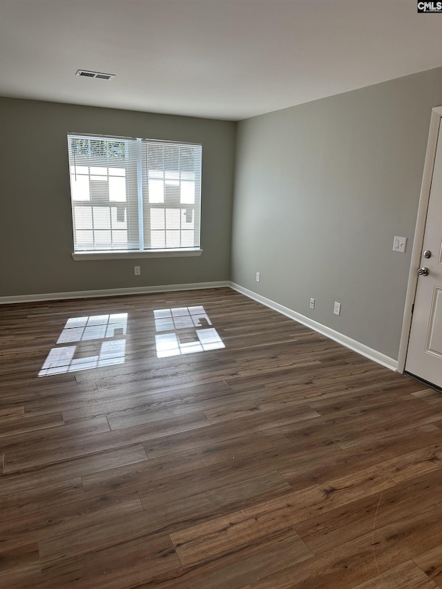 unfurnished room featuring visible vents, dark wood-type flooring, and baseboards