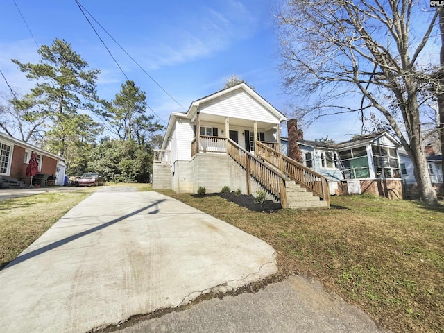 view of front facade featuring a front lawn, a porch, stairway, concrete driveway, and a chimney