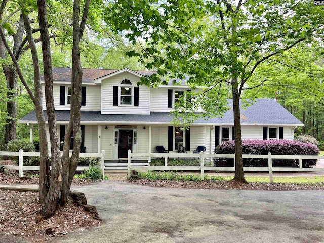 traditional home with covered porch, a fenced front yard, and roof with shingles