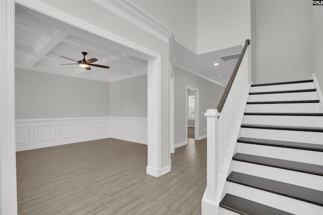 staircase featuring a ceiling fan, wood finished floors, coffered ceiling, crown molding, and beamed ceiling