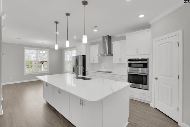 kitchen featuring a sink, appliances with stainless steel finishes, white cabinetry, wall chimney exhaust hood, and a kitchen island with sink