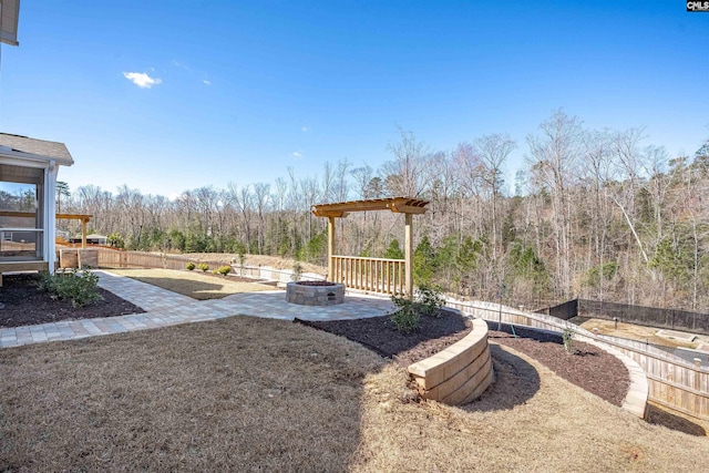 view of yard featuring a patio, a fire pit, fence, and a wooded view