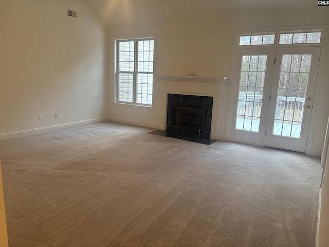 unfurnished living room featuring carpet flooring, vaulted ceiling, a fireplace with flush hearth, and visible vents