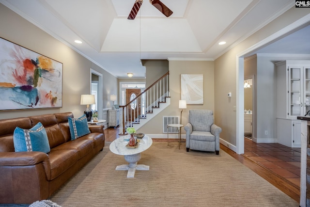 living area featuring crown molding, a raised ceiling, stairs, and wood finished floors