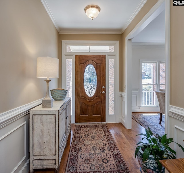 foyer entrance featuring wood finished floors, ornamental molding, wainscoting, and a decorative wall