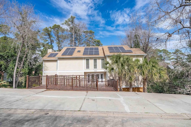 view of front facade with fence, roof mounted solar panels, and a chimney