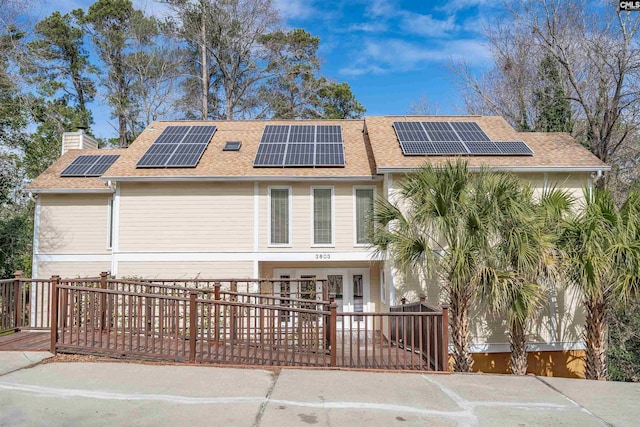 rear view of house featuring roof with shingles, solar panels, and a chimney