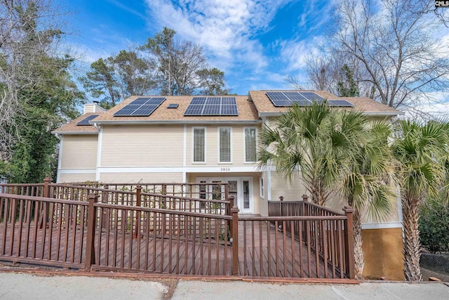 view of front facade featuring roof mounted solar panels, fence, a chimney, and a shingled roof