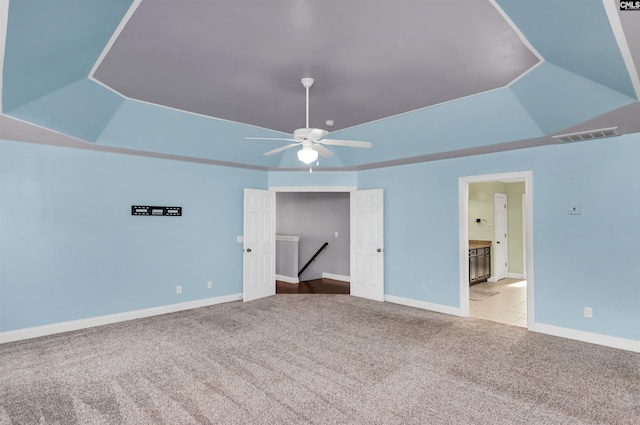 carpeted spare room with a tray ceiling, baseboards, visible vents, and ceiling fan