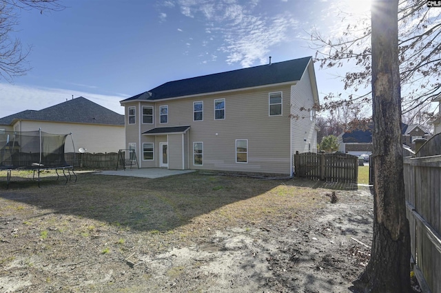 rear view of property featuring fence, a trampoline, and a patio area