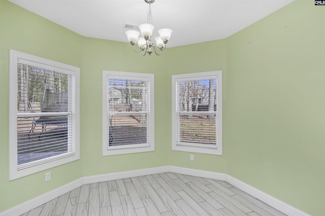 spare room featuring light wood-type flooring, visible vents, baseboards, and a chandelier