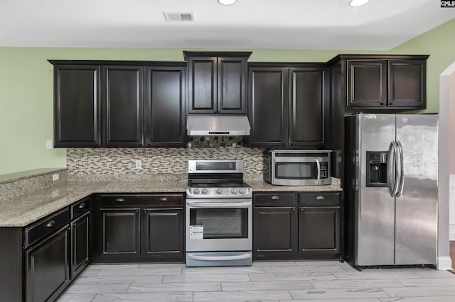 kitchen with under cabinet range hood, light stone counters, tasteful backsplash, appliances with stainless steel finishes, and a peninsula