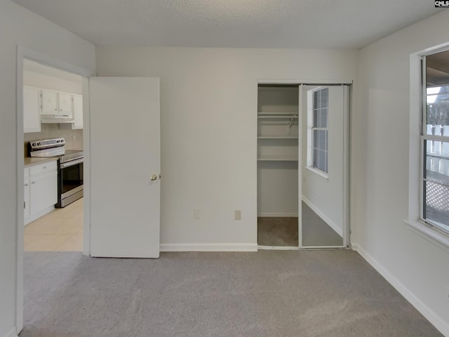 unfurnished bedroom featuring a closet, light colored carpet, a textured ceiling, and baseboards