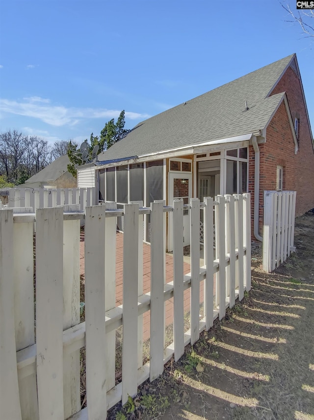 exterior space featuring a sunroom, fence, brick siding, and roof with shingles