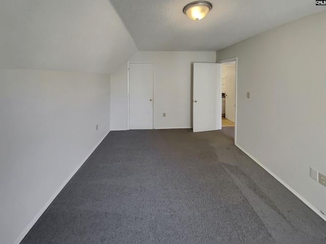 interior space featuring vaulted ceiling, carpet flooring, baseboards, and a textured ceiling