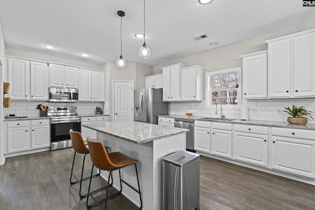 kitchen with visible vents, dark wood-style flooring, a sink, appliances with stainless steel finishes, and a kitchen bar