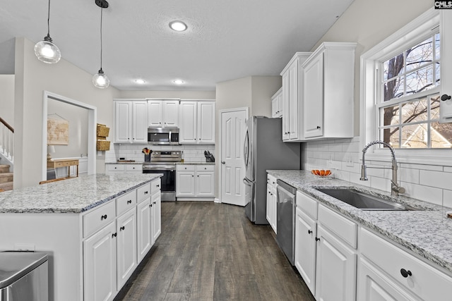 kitchen with dark wood finished floors, a sink, hanging light fixtures, white cabinets, and appliances with stainless steel finishes