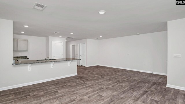 unfurnished living room with visible vents, dark wood-type flooring, baseboards, and a sink