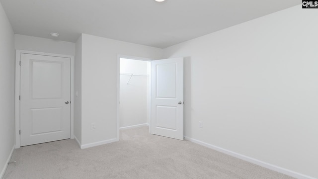 unfurnished bedroom with light carpet, a closet, a walk in closet, and baseboards