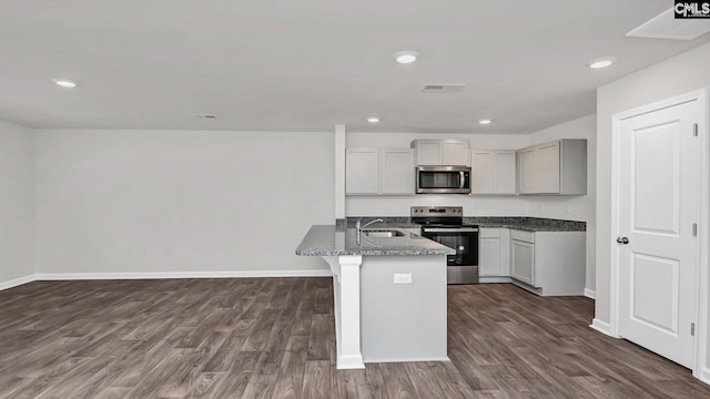 kitchen featuring visible vents, a sink, dark stone counters, stainless steel appliances, and dark wood-style flooring