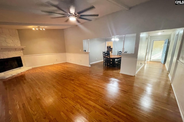 unfurnished living room with ceiling fan, baseboards, a stone fireplace, and wood finished floors