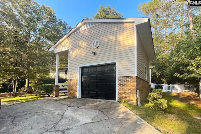 view of side of home featuring a garage, fence, brick siding, and driveway