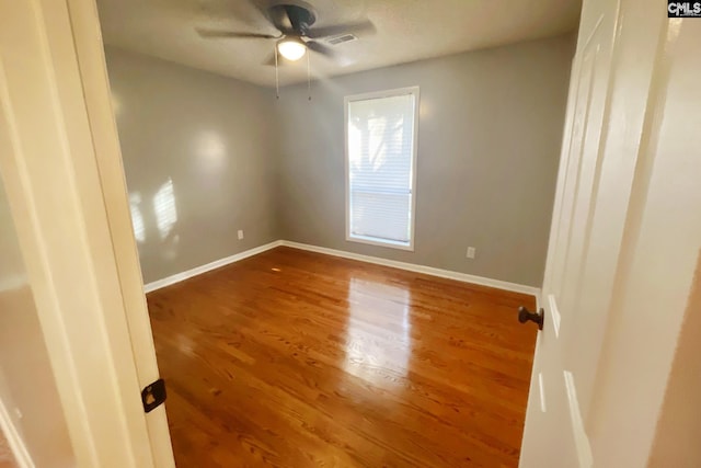 empty room featuring a ceiling fan, wood finished floors, visible vents, and baseboards