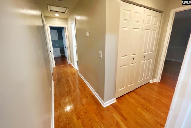 hall featuring light wood-style flooring, attic access, and baseboards